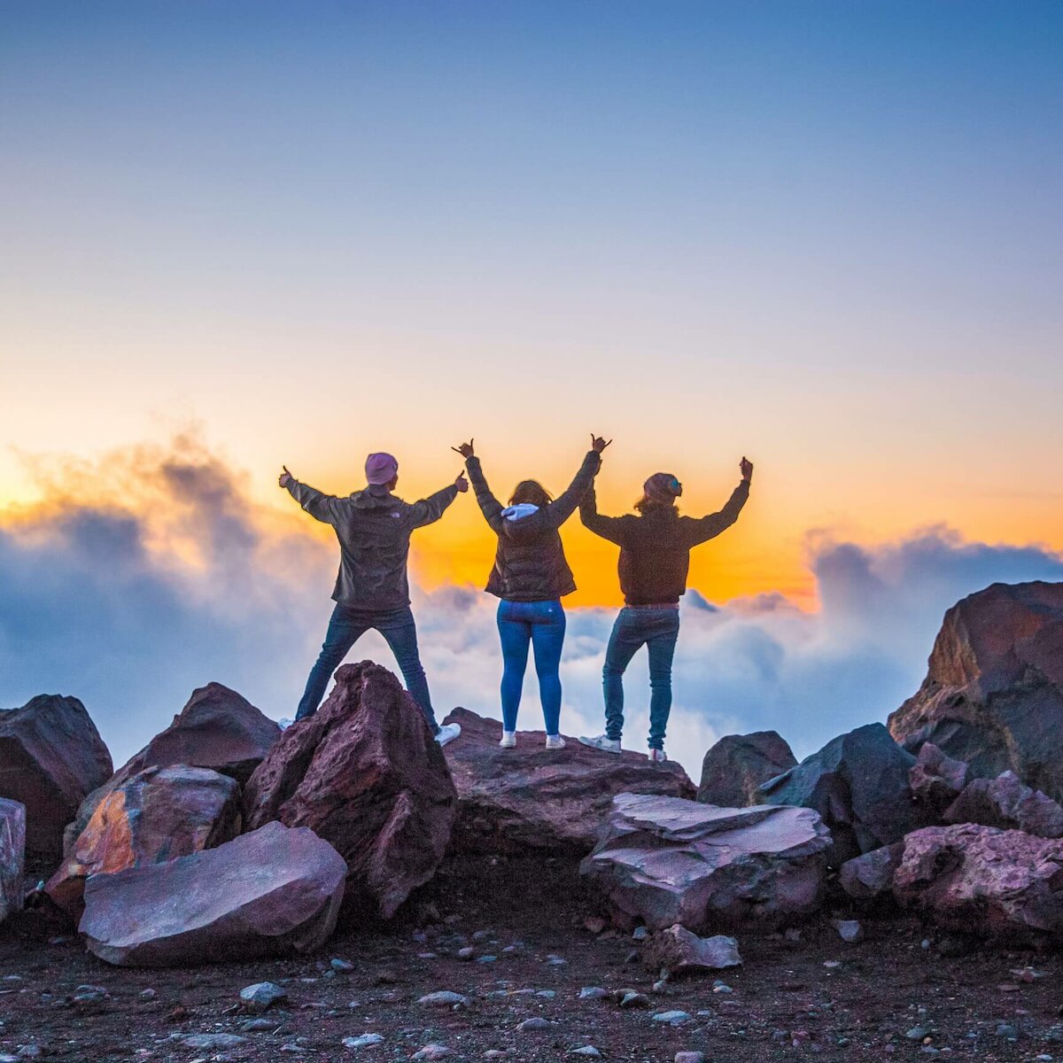 group with arms up with sunset and mountain in background
